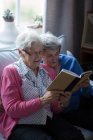 Amici anziani che leggono un libro insieme a casa — Foto stock
