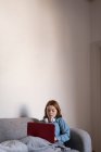 Donna che utilizza un computer portatile sul divano in soggiorno a casa — Foto stock