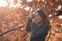 Jeune femme prenant des photos avec un appareil photo dans le parc — Photo de stock