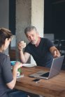 Бізнес-колеги обговорюють ноутбук під час сніданку в офісі — стокове фото