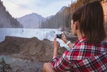 Visão traseira da mulher tirando foto de cachoeira com telefone celular — Fotografia de Stock
