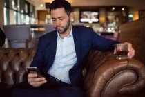 Businessman using while having whisky in hotel — Stock Photo