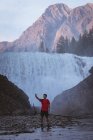 Young man taking selfie with mobile phone near waterfall — Stock Photo