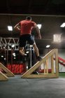Вид ззаду м'язистого чоловіка, що стрибає на похилих клинах у спортзалі — стокове фото