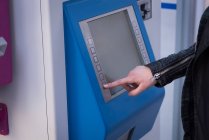 Sección media de la mujer utilizando la máquina expendedora de billetes en la estación - foto de stock