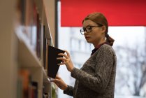 Jeune femme ramassant un livre à la bibliothèque — Photo de stock