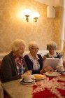 Senior friends using digital tablet while having breakfast at home — Stock Photo