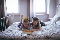 Schwestern lesen ein Buch auf dem Bett im Schlafzimmer — Stockfoto
