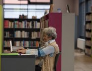 Активная пожилая женщина с ноутбуком в библиотеке — стоковое фото