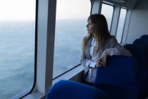 Beautiful woman looking through window while sailing in cruise ship — Stock Photo