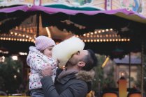 Батько і дочка мають бавовняні цукерки в сутінках в парку розваг — стокове фото