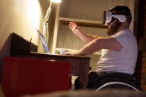 Homem com deficiência em fone de ouvido de realidade virtual usando laptop em casa — Fotografia de Stock