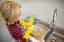Niño lavando utensilio en la cocina en casa - foto de stock