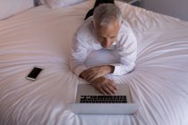 Uomo d'affari che utilizza un computer portatile sul letto in camera d'albergo — Foto stock