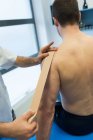 Fisioterapeuta aplicando bandagem no ombro do paciente na clínica — Fotografia de Stock