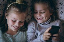 Geschwister benutzen Handy auf Bett im Schlafzimmer — Stockfoto