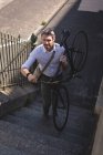 Homem carregando bicicleta e andando no andar de cima em um dia ensolarado — Fotografia de Stock