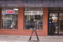 Молодой человек пользуется мобильным телефоном у входа в магазин — стоковое фото