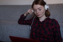 Jovem mulher ouvindo música com seu laptop na sala de estar — Fotografia de Stock