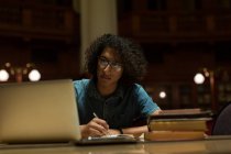 Giovane che studia con computer portatile in biblioteca — Foto stock