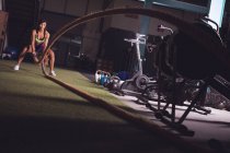 Adatta donna che fa esercizio di corda da battaglia in palestra — Foto stock