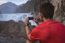 Вид ззаду чоловіка, фотографія водоспаду з мобільним телефоном — стокове фото