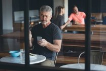 Empresário usando telefone celular enquanto toma café da manhã no escritório — Fotografia de Stock