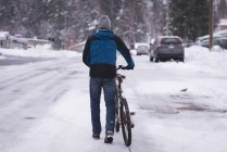 Вид ззаду людини, що йде з велосипедом на засніженій вулиці — стокове фото