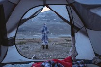 Вид сзади на человека, завернутого в одеяло возле палатки — стоковое фото