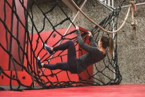 Mulher muscular escalando uma cerca de corda no ginásio — Fotografia de Stock