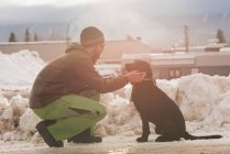 Homme caressant son chien sur le côté de la rue en hiver — Photo de stock