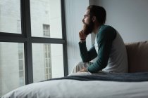 Man looking through window in bedroom at home — Stock Photo