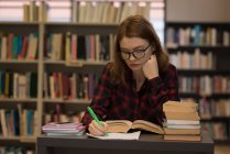 Mujer joven escribiendo en papel en la biblioteca - foto de stock