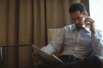 Empresário lendo jornal enquanto bebe uísque no quarto de hotel — Fotografia de Stock