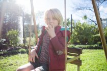 Мальчик расслабляется в качели в солнечный день в саду — стоковое фото