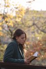 Jeune femme lisant un livre dans le parc — Photo de stock