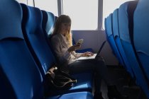 Frau checkt Handy, während sie Laptop im Kreuzfahrtschiff benutzt — Stockfoto