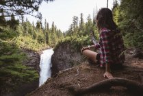 Visão traseira da mulher sentada perto da cachoeira — Fotografia de Stock