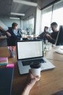 Бизнесмен пьет кофе, пока коллеги обсуждают в офисе — стоковое фото