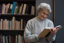 Donna anziana attiva che legge un libro in biblioteca — Foto stock
