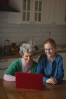 Бабушка и внучка используют ноутбук на кухне дома — стоковое фото