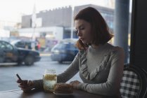 Вид сбоку женщины, пользующейся мобильным телефоном в кафе — стоковое фото