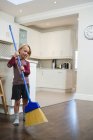 Niño piso de limpieza con escoba en la cocina en casa - foto de stock