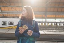 Mulher usando telefone celular ao ter comida envolvente na estação ferroviária — Fotografia de Stock