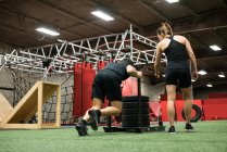 Treinador feminino ajudando o homem com trenó empurrando no estúdio de fitness — Fotografia de Stock