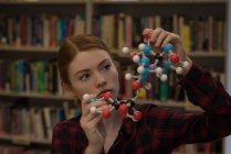 Молода жінка аналізує модель молекули в бібліотеці — стокове фото
