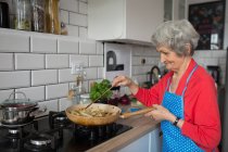 Donna anziana cucina cibo in cucina a casa — Foto stock