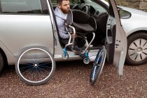 Інвалідний молодий чоловік тримає інвалідне крісло під час посадки в машину — стокове фото