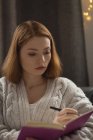 Mujer escribiendo en un diario en la sala de estar en casa - foto de stock