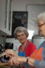 Старші друзі взаємодіють, готуючи їжу на кухні вдома — стокове фото